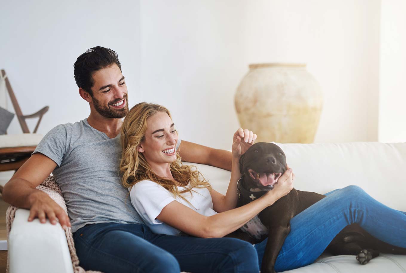 man and woman in casual attire sitting together on couch with a dog